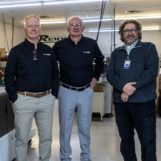 three production print professionals smiling by a commercial printer